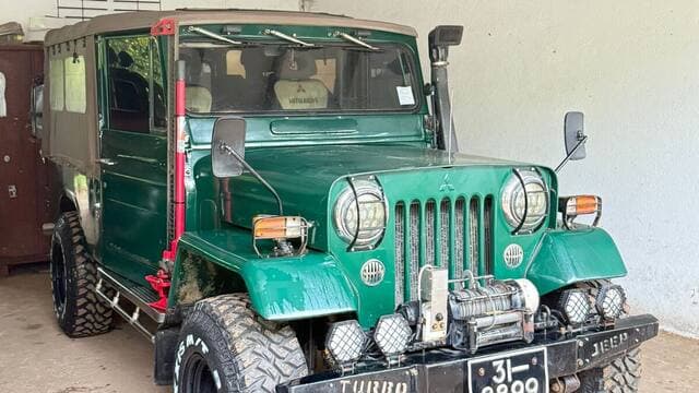 Green Mitsubishi jeep with off-road tyres in a carport